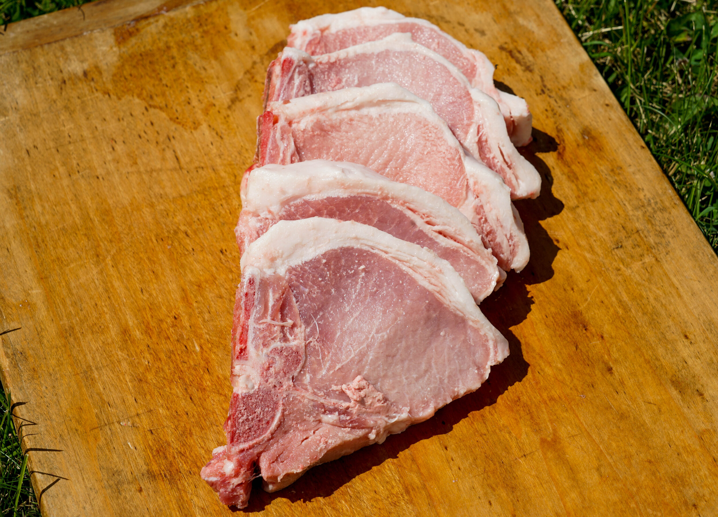 Freshly cut pork chops arranged on a wooden cutting board, showcasing their marbled texture and pink color, ideal for grilling or cooking. Perfect for meat recipes and culinary presentations.