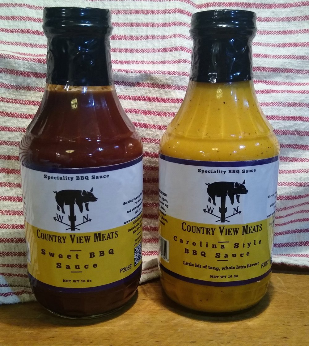 Bottles of Country View Meats BBQ sauces featuring Sweet BBQ Sauce and Carolina Style BBQ Sauce, placed on a wooden surface with a striped cloth background. Each bottle contains 16 oz and highlights unique flavors for grilling enthusiasts.