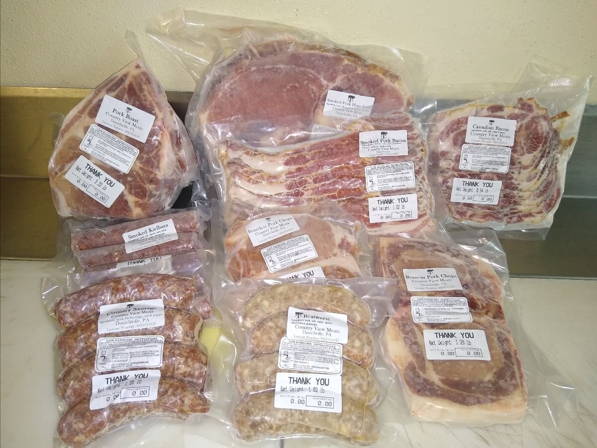 Assorted vacuum-sealed meats including pork roasts, smoked bacon, kielbasa, and pork chops from Country View Meats, neatly arranged with labels indicating weight and product type.